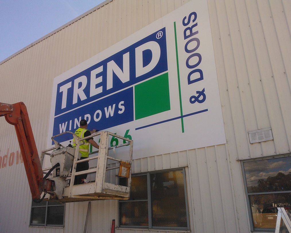 A man in a crane is painting a large sign for trend windows and doors A man in a crane is painting a large sign for trend windows and doors