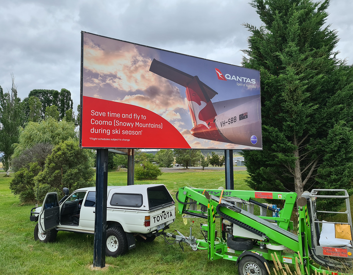 A white truck is parked in front of a large billboard. A white truck is parked in front of a large billboard.