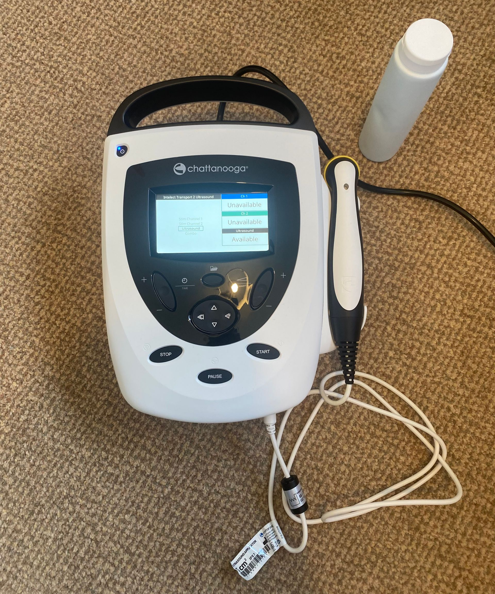 White ultrasound machine with attached probe and gel bottle.