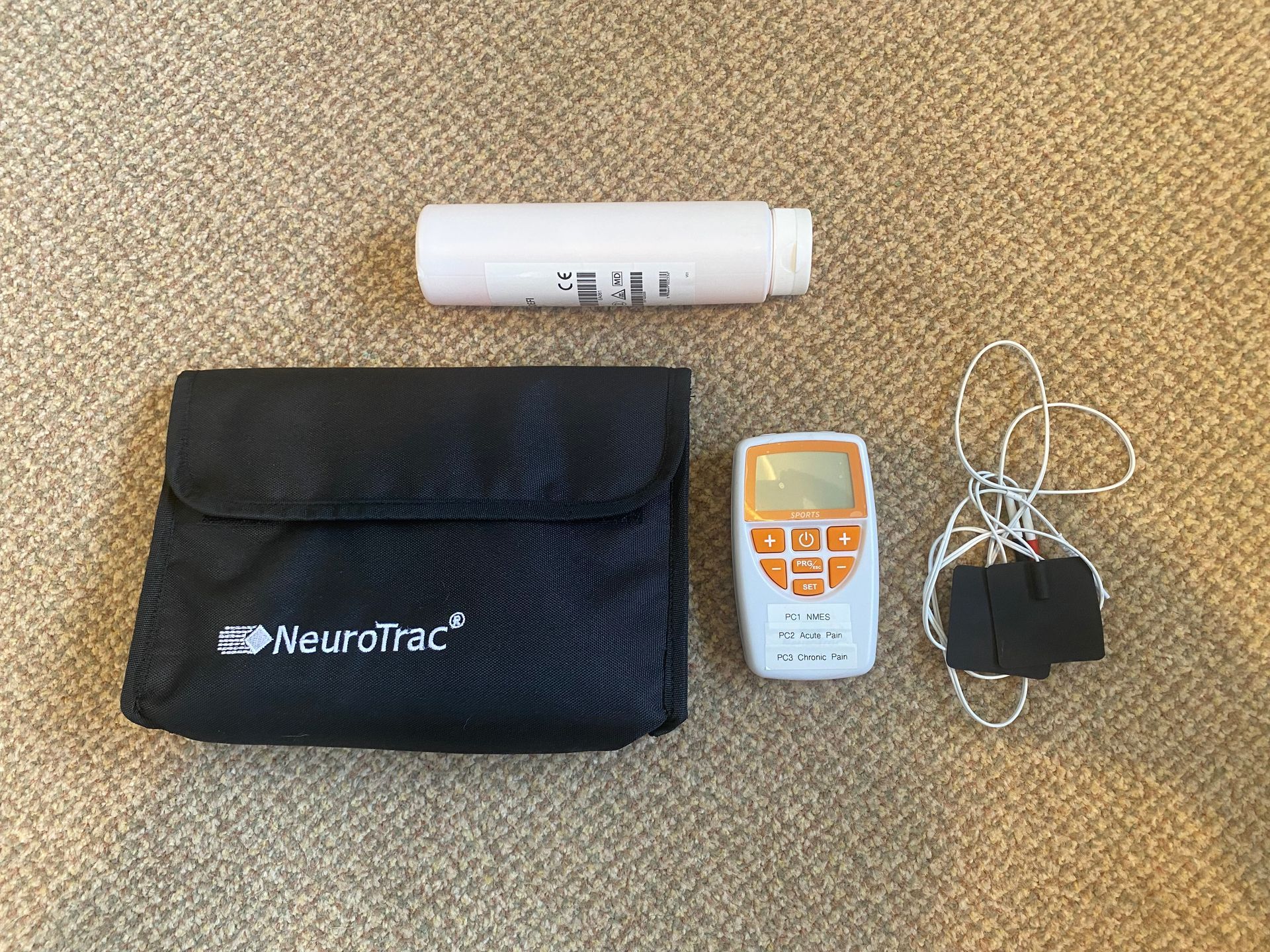 A NeuroTrac pelvic floor exerciser kit on a beige surface, including a controller, leads, electrodes, and a carry case.