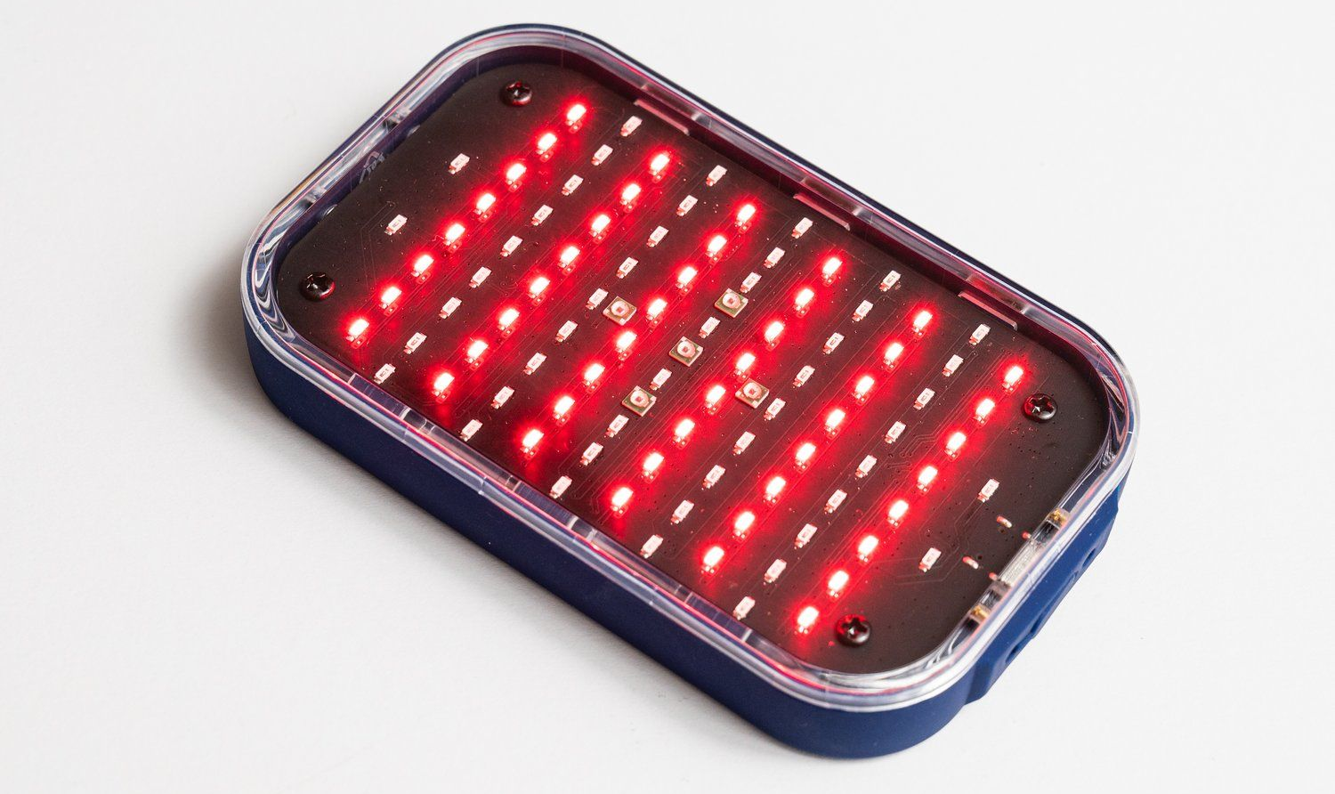 Rectangular red light therapy device, emitting bright red light, on a white surface.