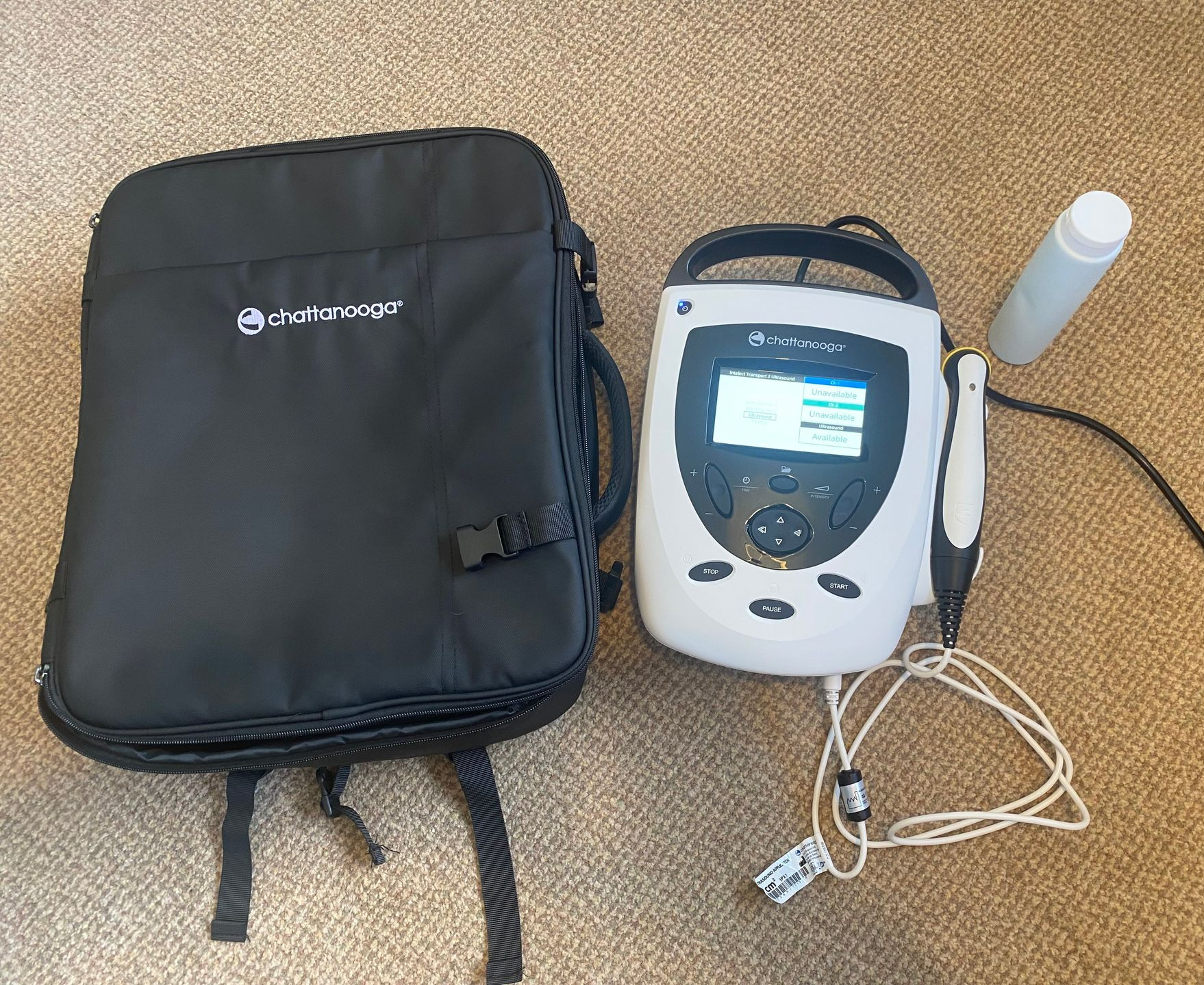 White medical device with screen and gel, next to a black bag.