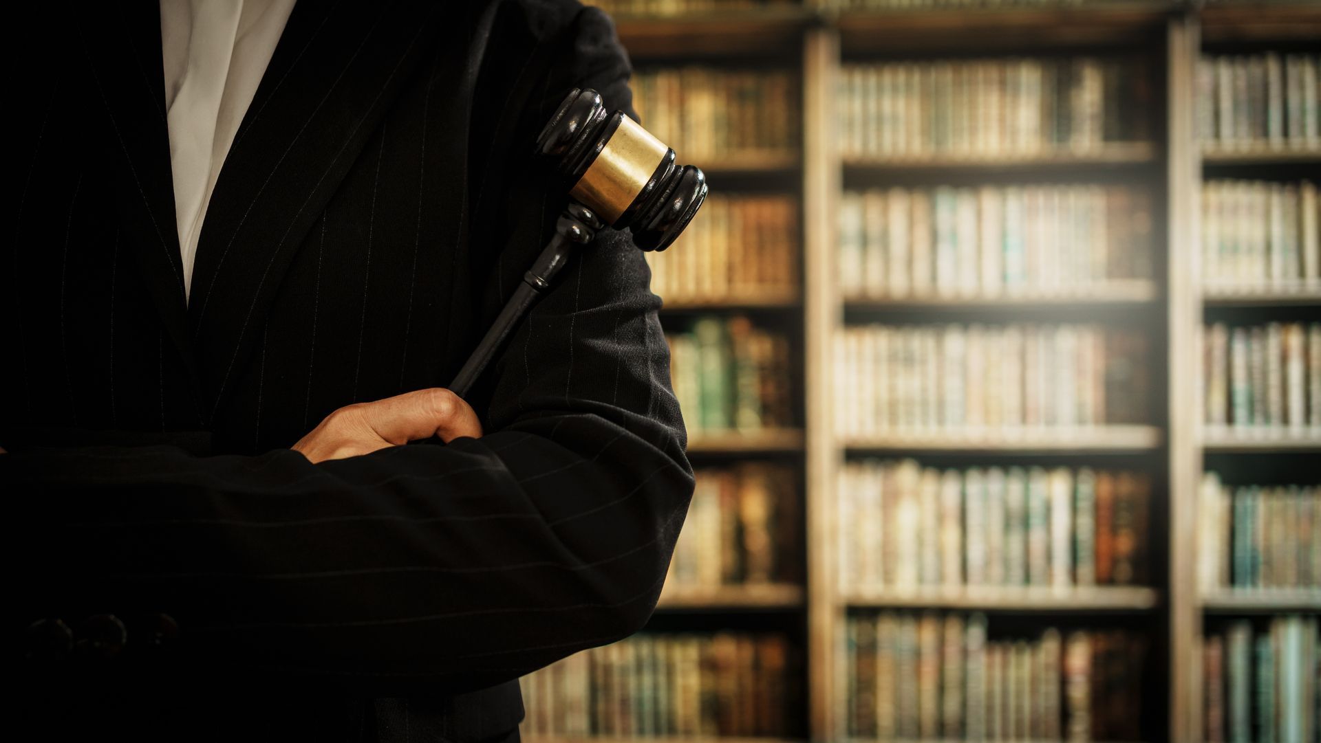 Person in suit holding gavel with bookshelves in background.