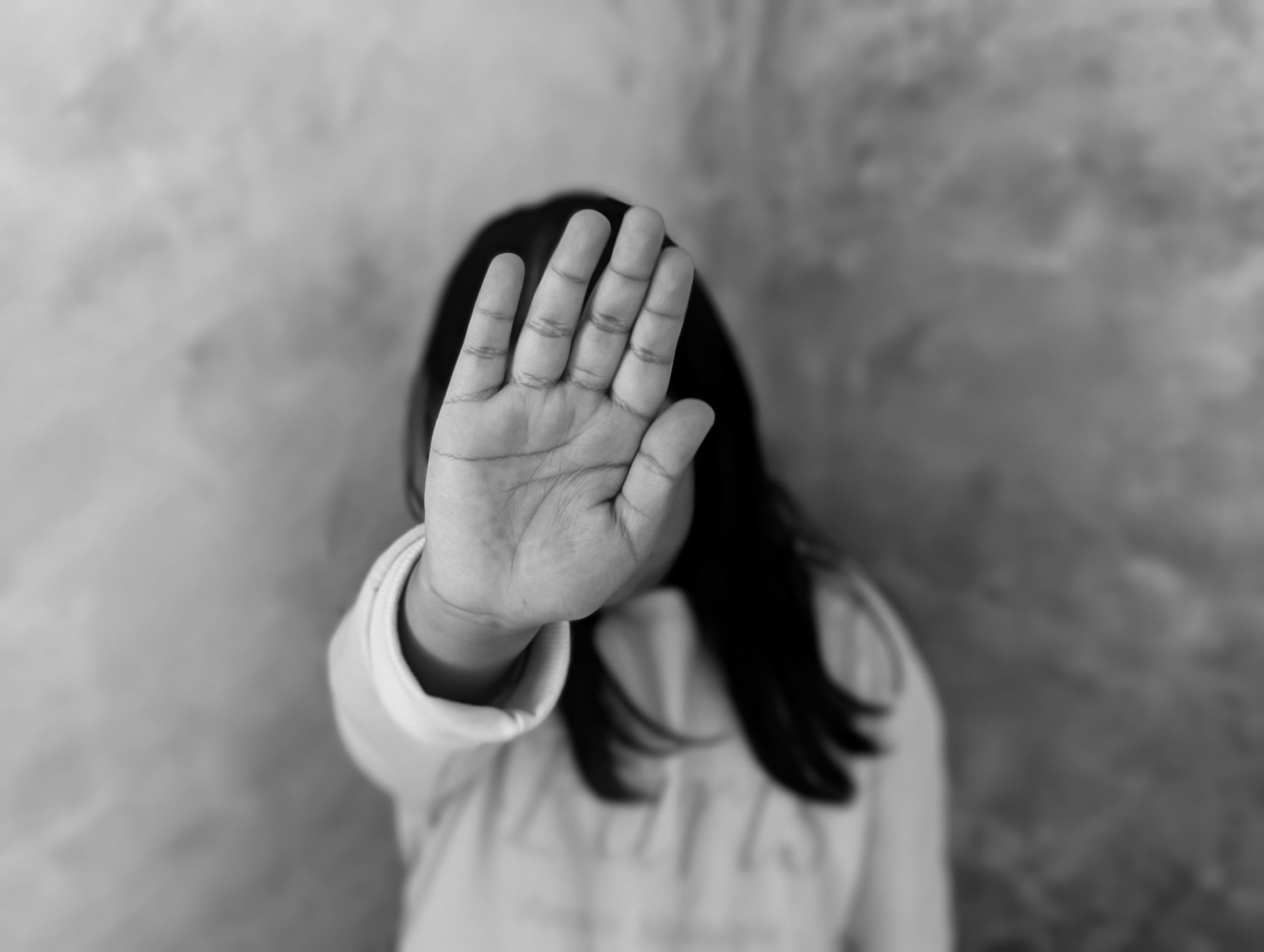 Person holds up hand, palm forward in a stop gesture, obscuring face; plain background.