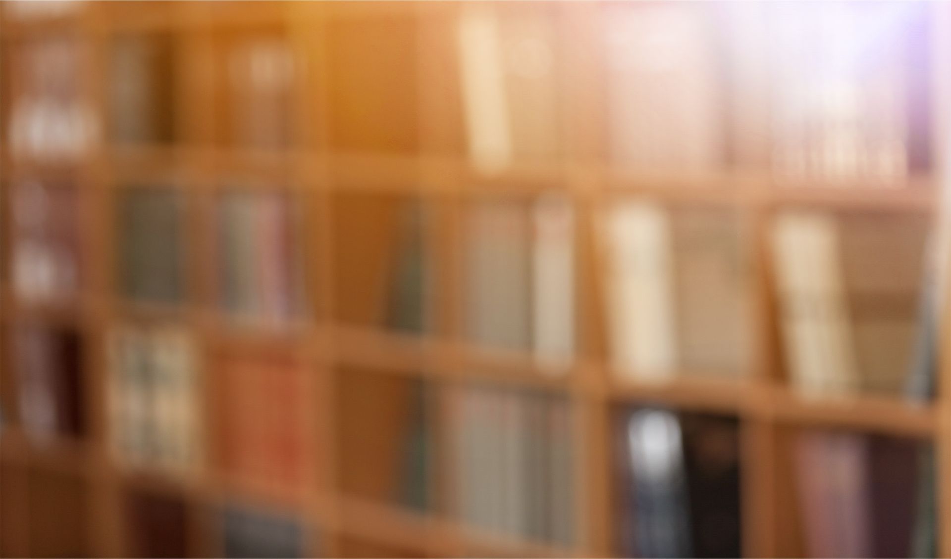 Bookshelves filled with books, slightly out of focus. Wooden shelves. Warm sunlight.