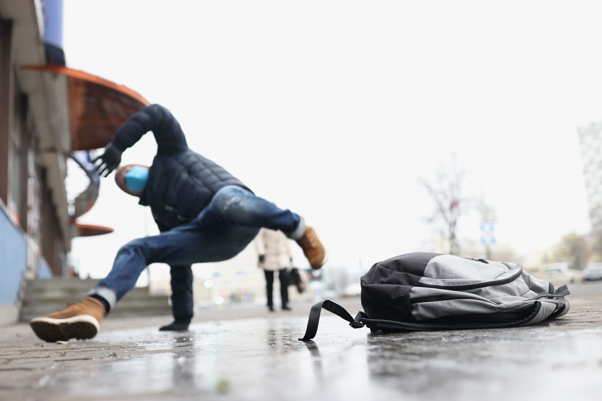 Person slipping on wet pavement, backpack on ground near building.