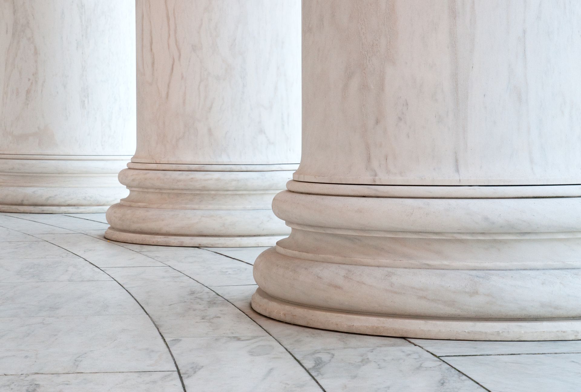 Three white marble columns with ornate bases, on a marble floor.