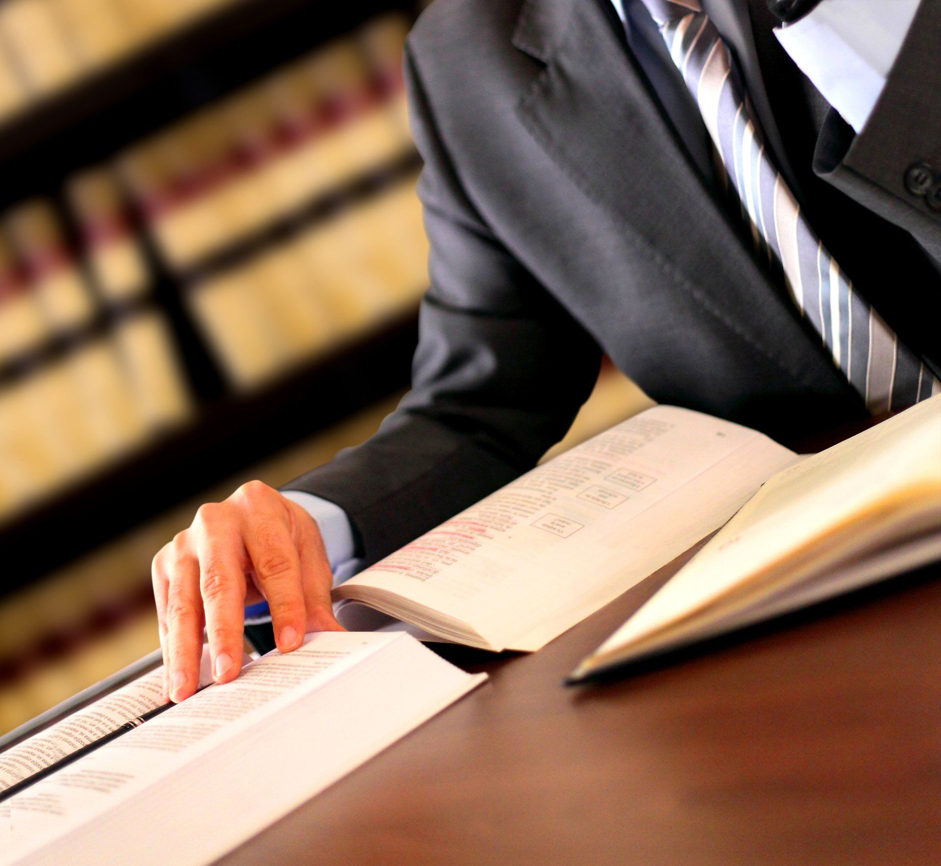 Person in suit reading documents at a desk, with bookshelves in background.