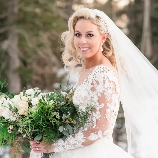 Bridesmaid helping the bride put on cowboy boots in a room with a mirror and couch.