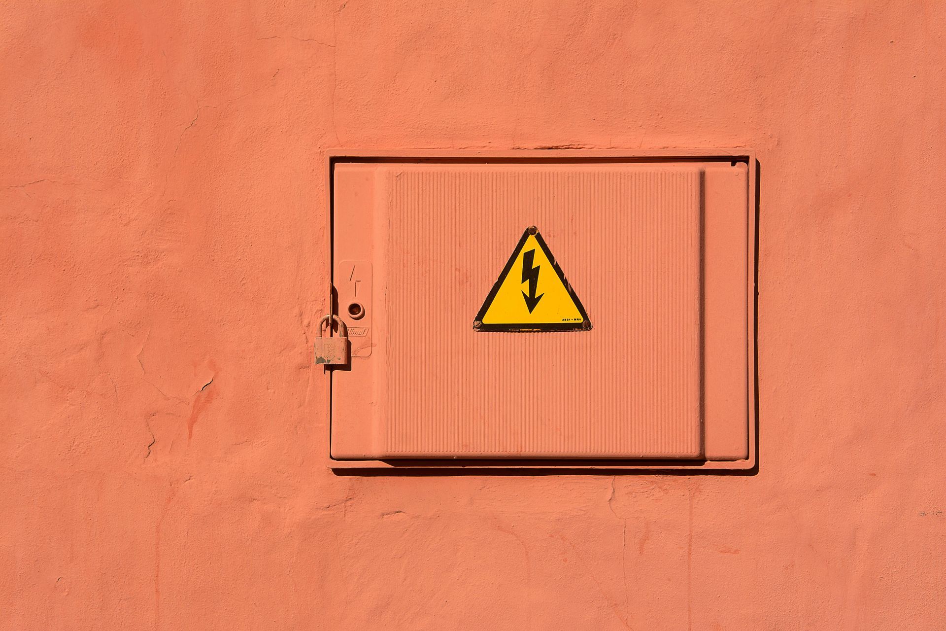 A yellow triangle with a lightning bolt on it is on a red wall.