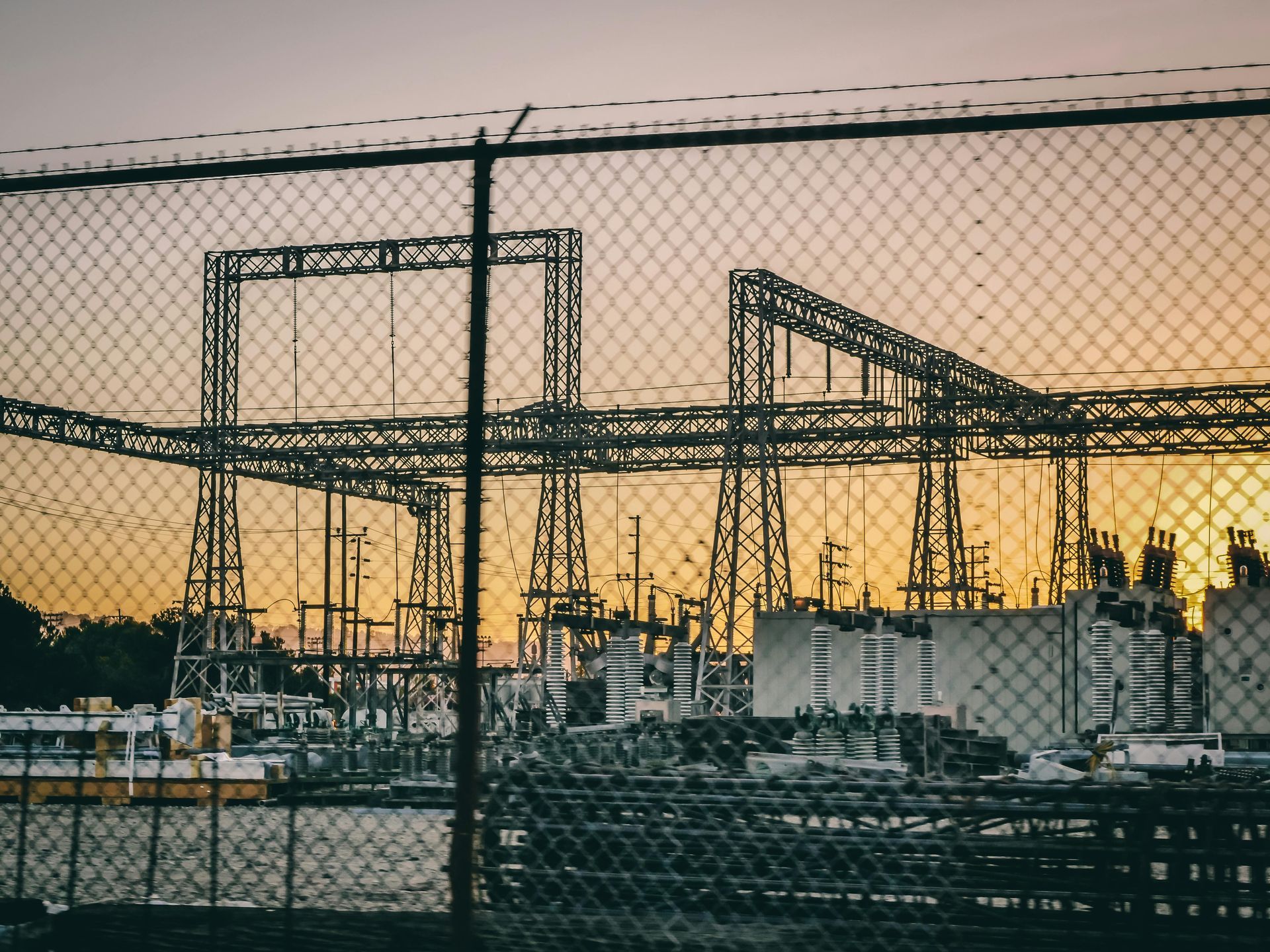 A chain link fence surrounds a power plant at sunset.