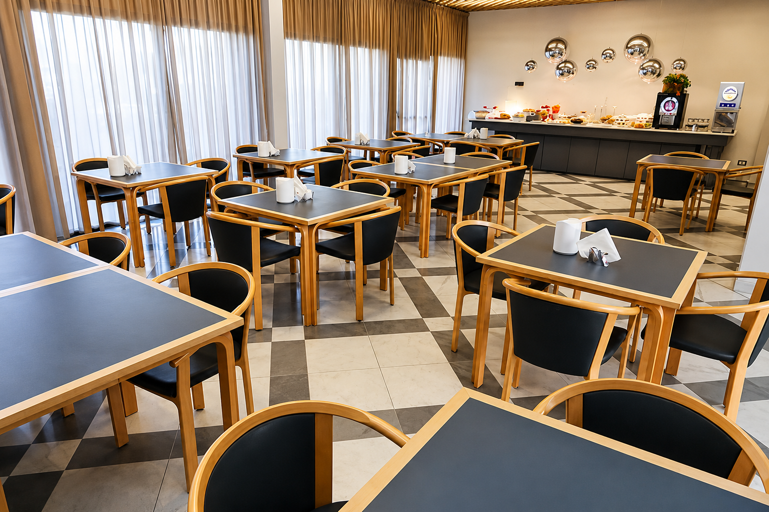 Sala da pranzo vuota di un ristorante con sedie di legno, tavoli scuri e tende trasparenti alle grandi finestre.