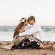A bride and groom are kissing on the beach . the bride is wearing a flower crown.