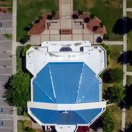 An aerial view of a large building with a blue roof surrounded by trees and a parking lot.