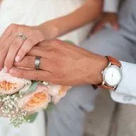 A bride and groom are holding hands and the bride has a wedding ring on her finger.