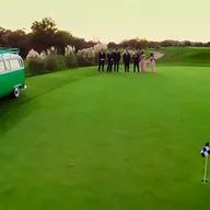 A group of people are standing on a golf course next to a green van.