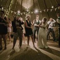 A group of people are dancing in a tent at a wedding reception.