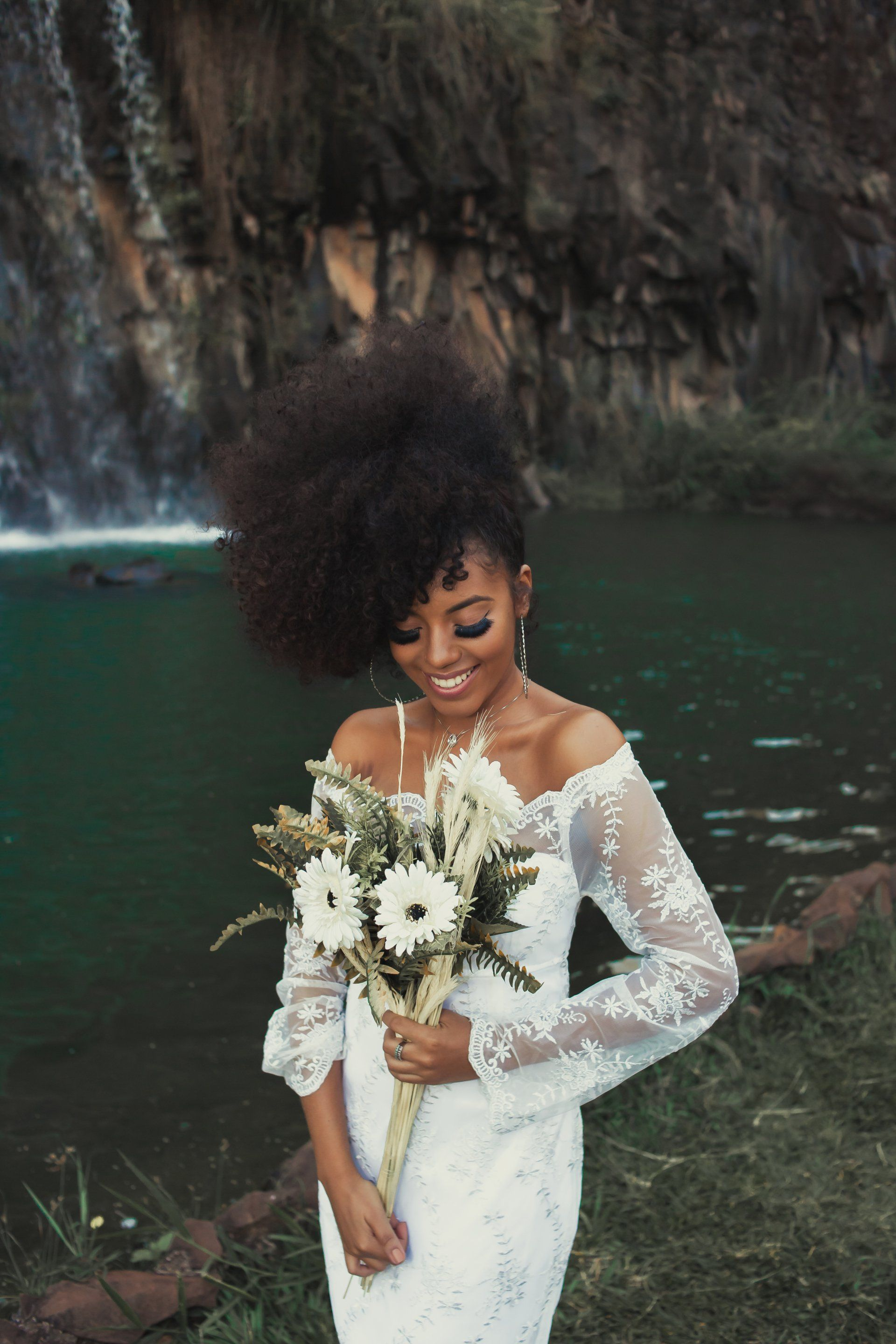 A woman in a wedding dress is holding a bouquet of flowers in front of a waterfall.