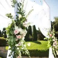 A white arch decorated with flowers and greenery for a wedding ceremony.