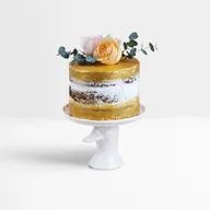 A gold cake with flowers on top of it on a white cake stand.