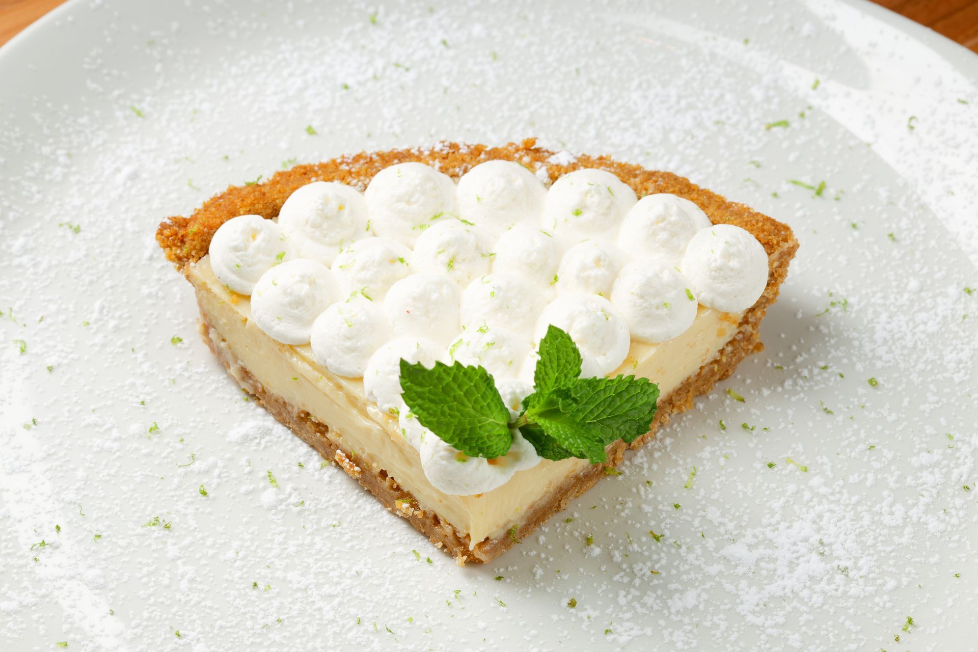 A slice of key lime pie with whipped cream and mint leaves on a white plate.