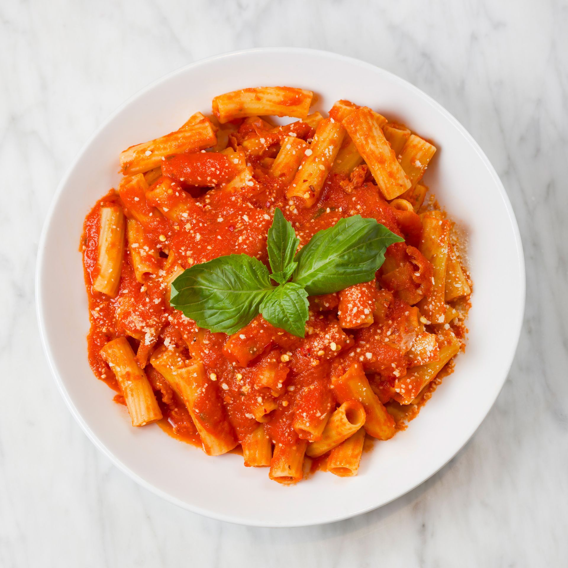 A bowl of pasta with tomato sauce and basil on a table.