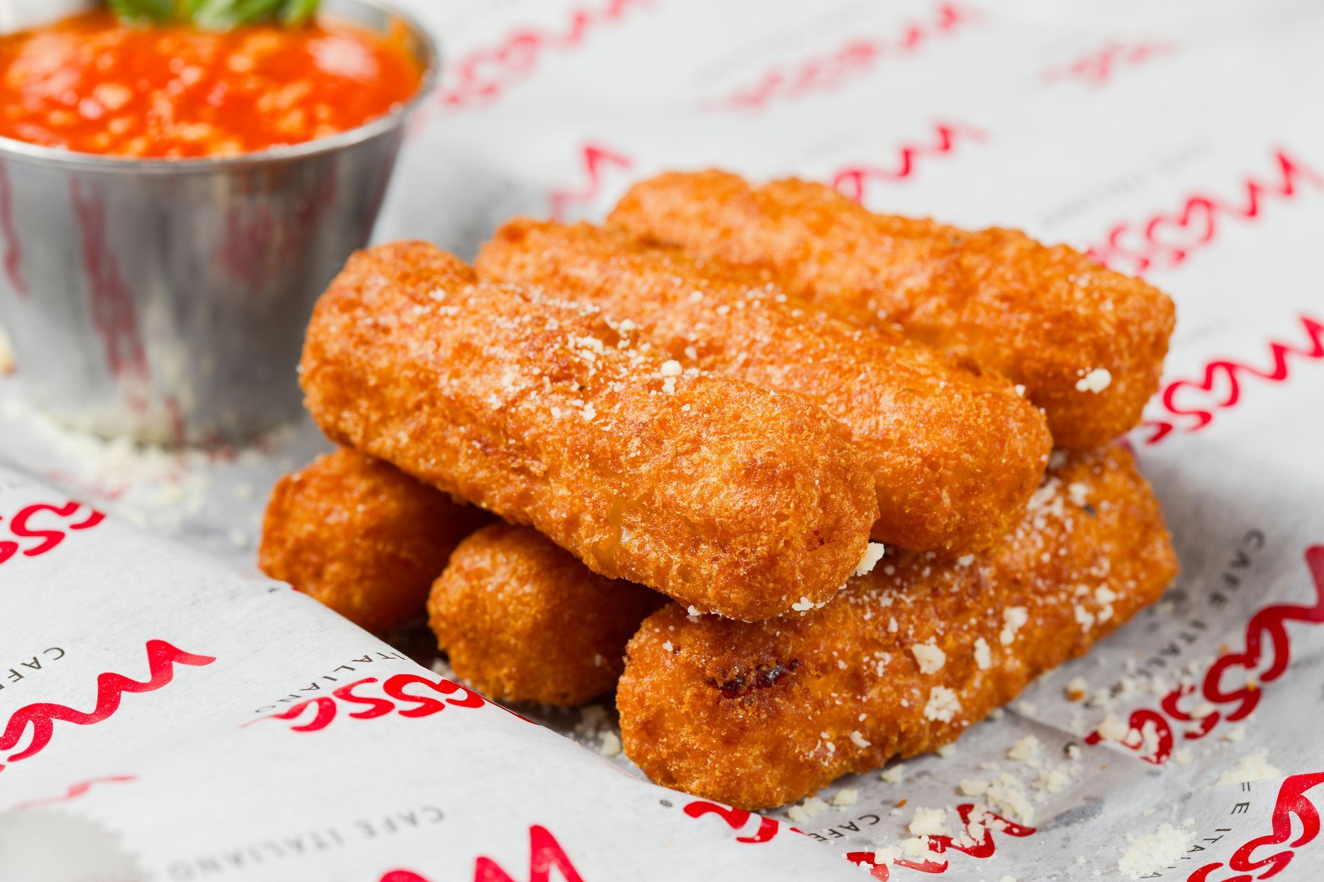 A stack of mozzarella sticks on a table next to a bowl of sauce.