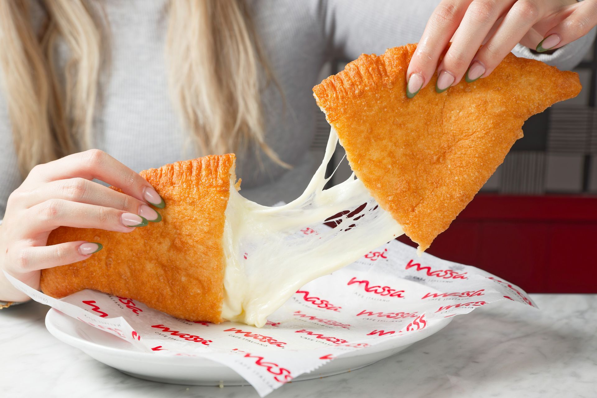 A woman is eating a fried pastry with cheese coming out of it.