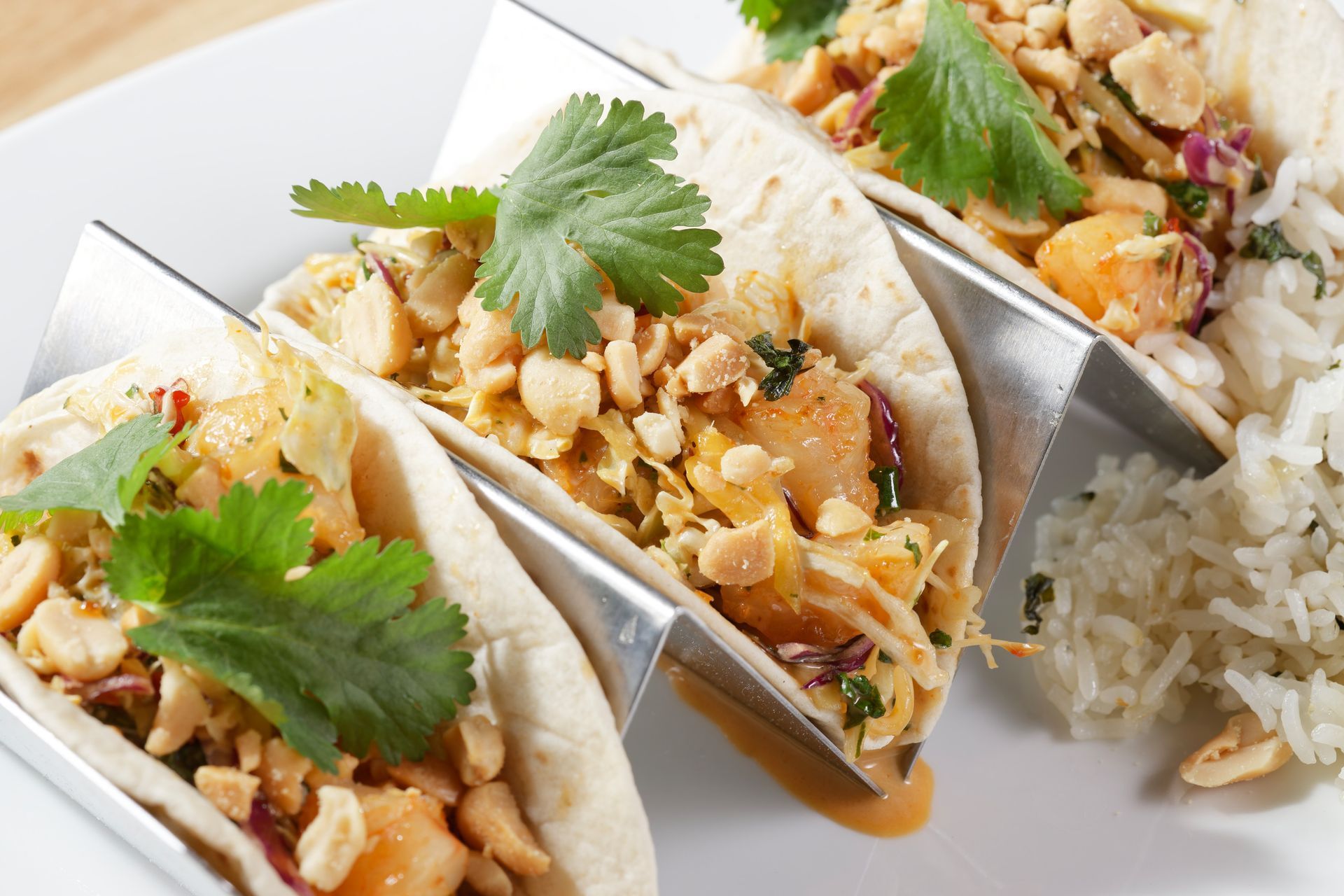 A white plate topped with three tacos and rice