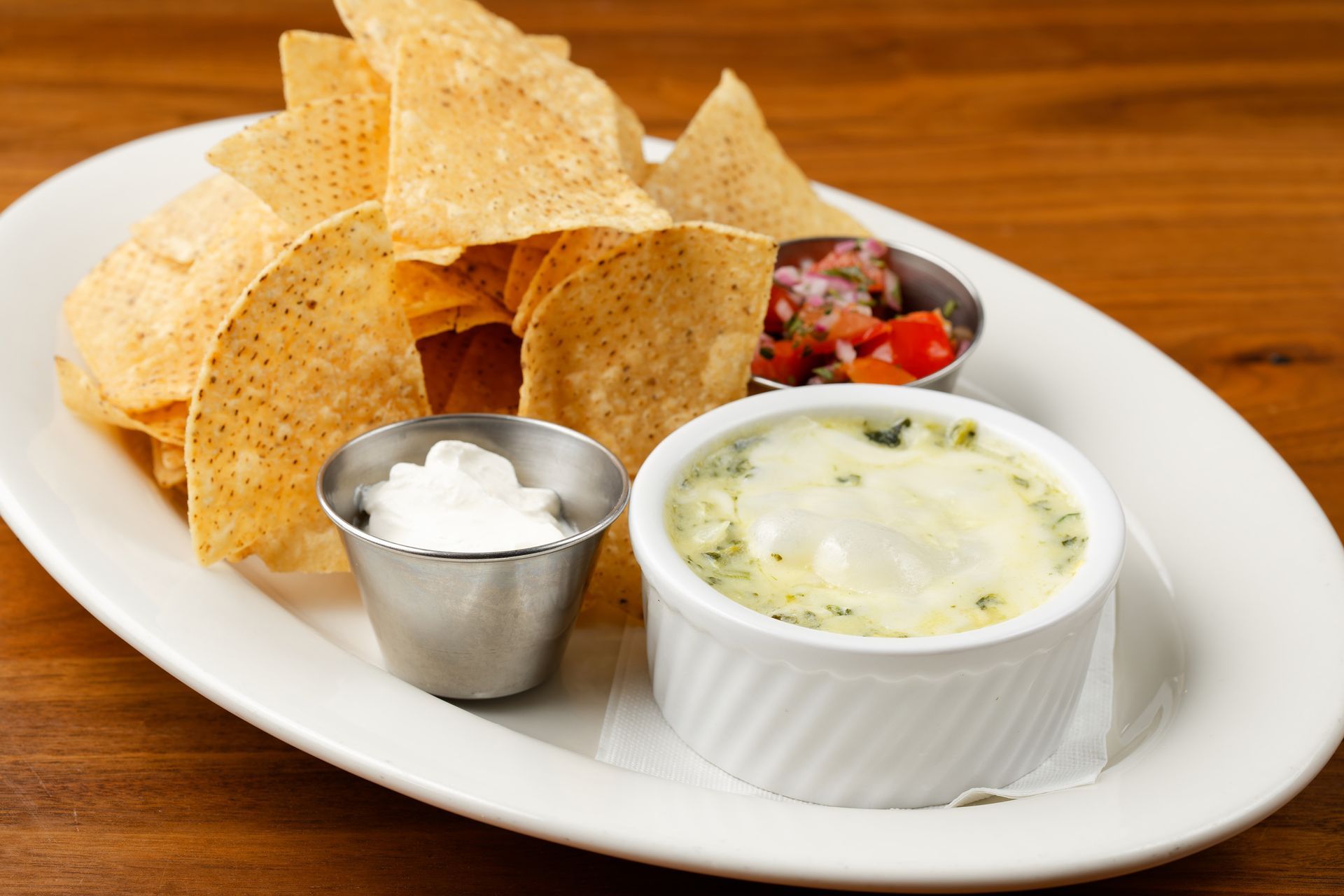 A plate of tortilla chips and dip on a wooden table.