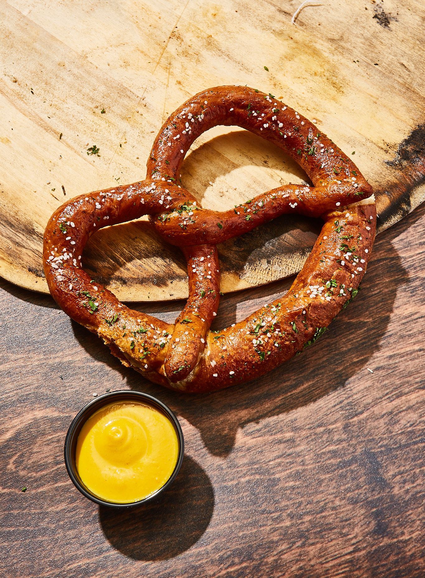 A pretzel is sitting on a wooden table next to a bowl of mustard.