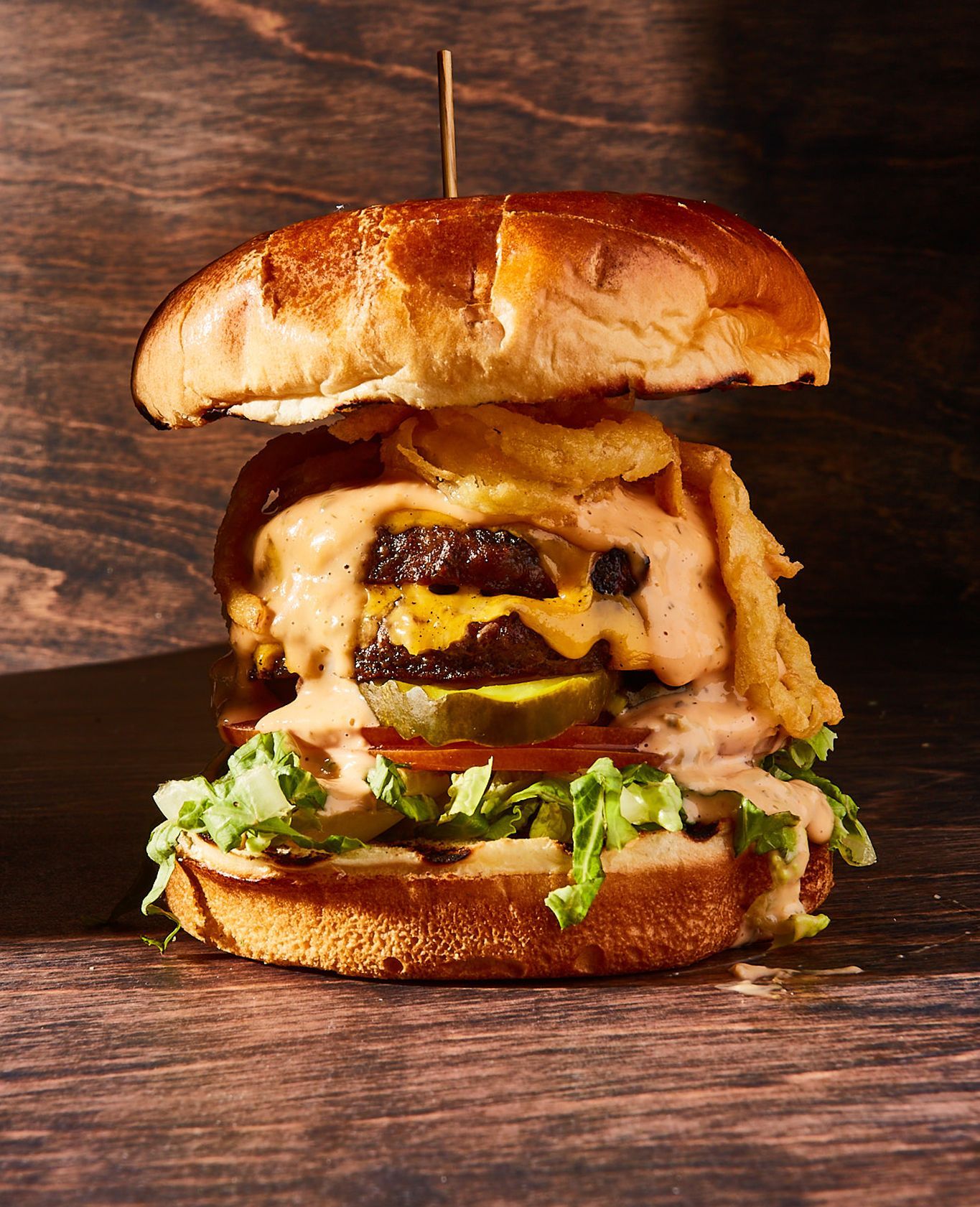 A hamburger is sitting on a wooden table with a toothpick sticking out of it.