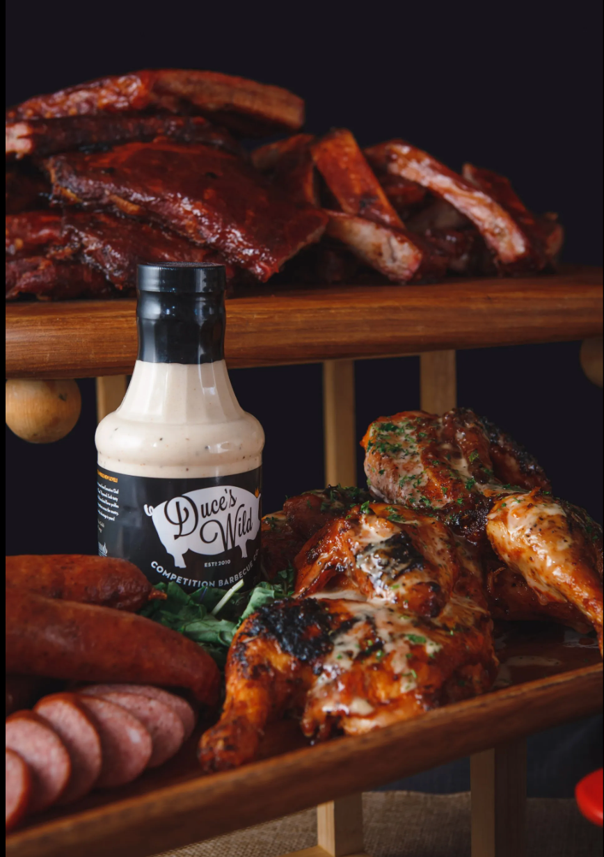 A bottle of sauce is sitting on a wooden shelf next to meat.