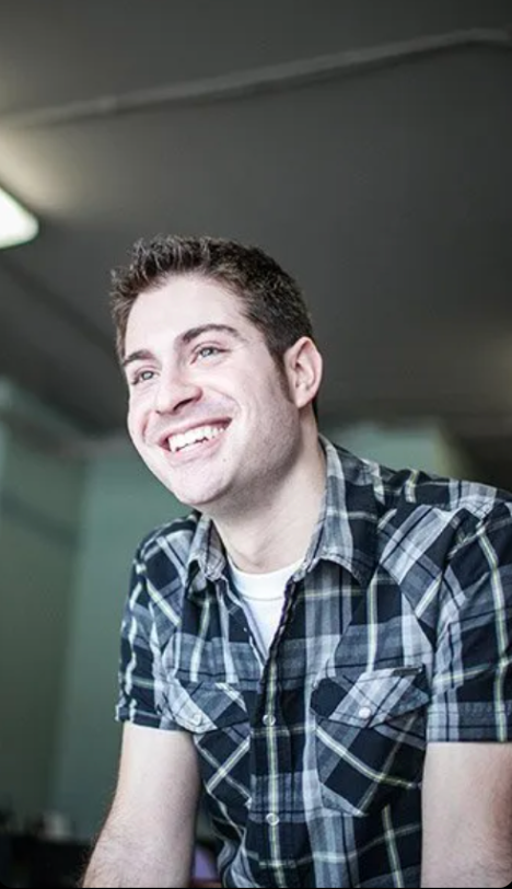 A man in a plaid shirt is smiling and looking away from the camera.