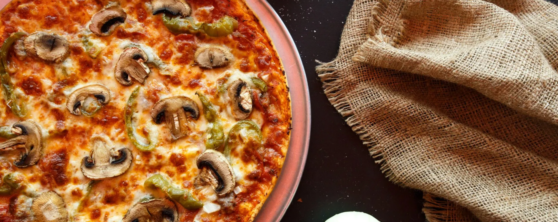 A pizza with mushrooms , peppers and cheese is sitting on a table next to a napkin.