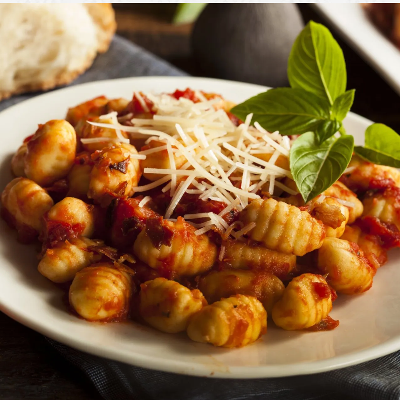 A plate of gnocchi with sauce and cheese on top