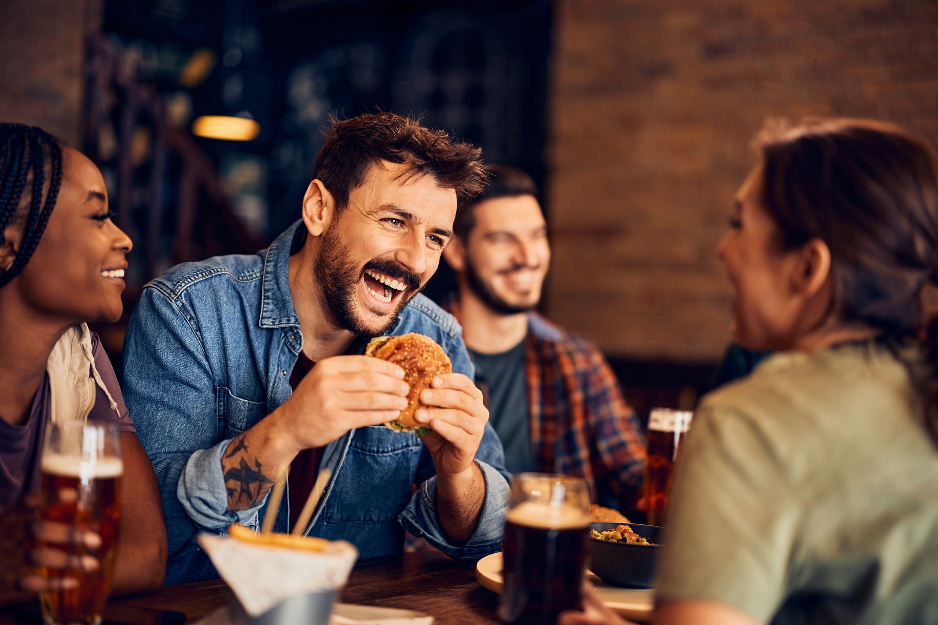 A group of people are sitting at a table in a restaurant eating hamburgers and drinking beer.