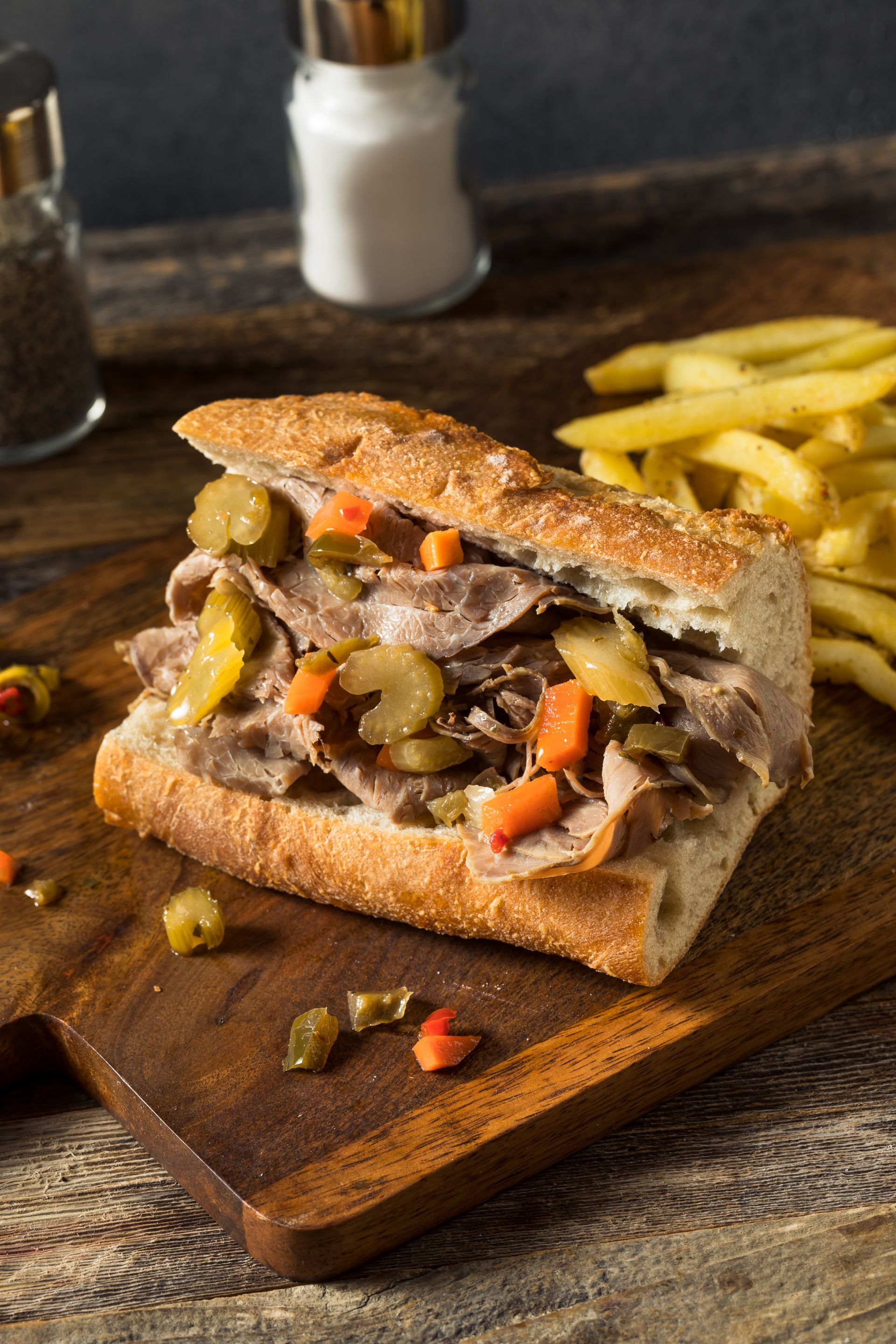 A roast beef sandwich is sitting on a wooden cutting board next to french fries.