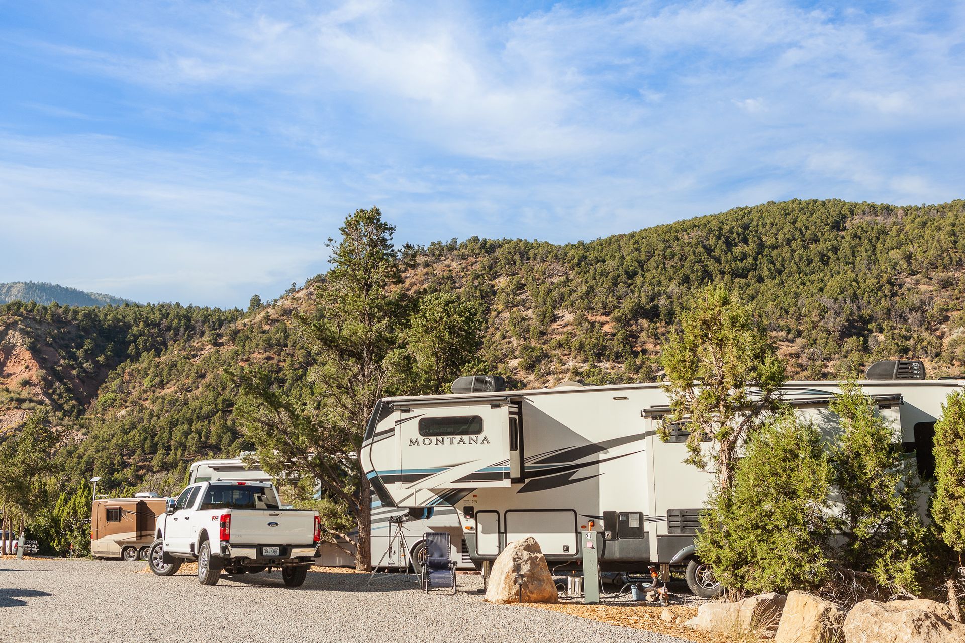 A group of rvs are parked in a gravel lot in front of a mountain.