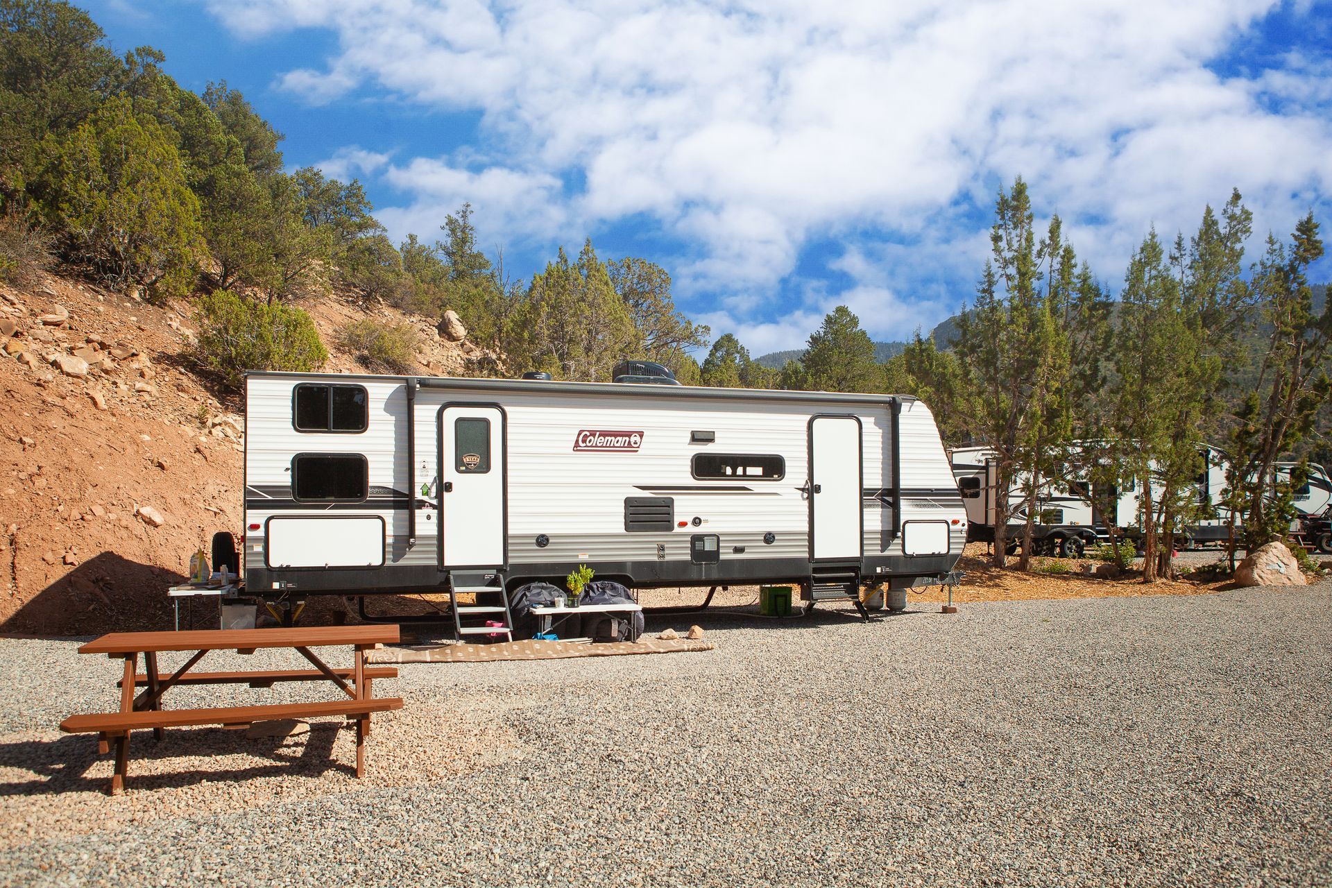 A rv is parked in a gravel area next to a picnic table.