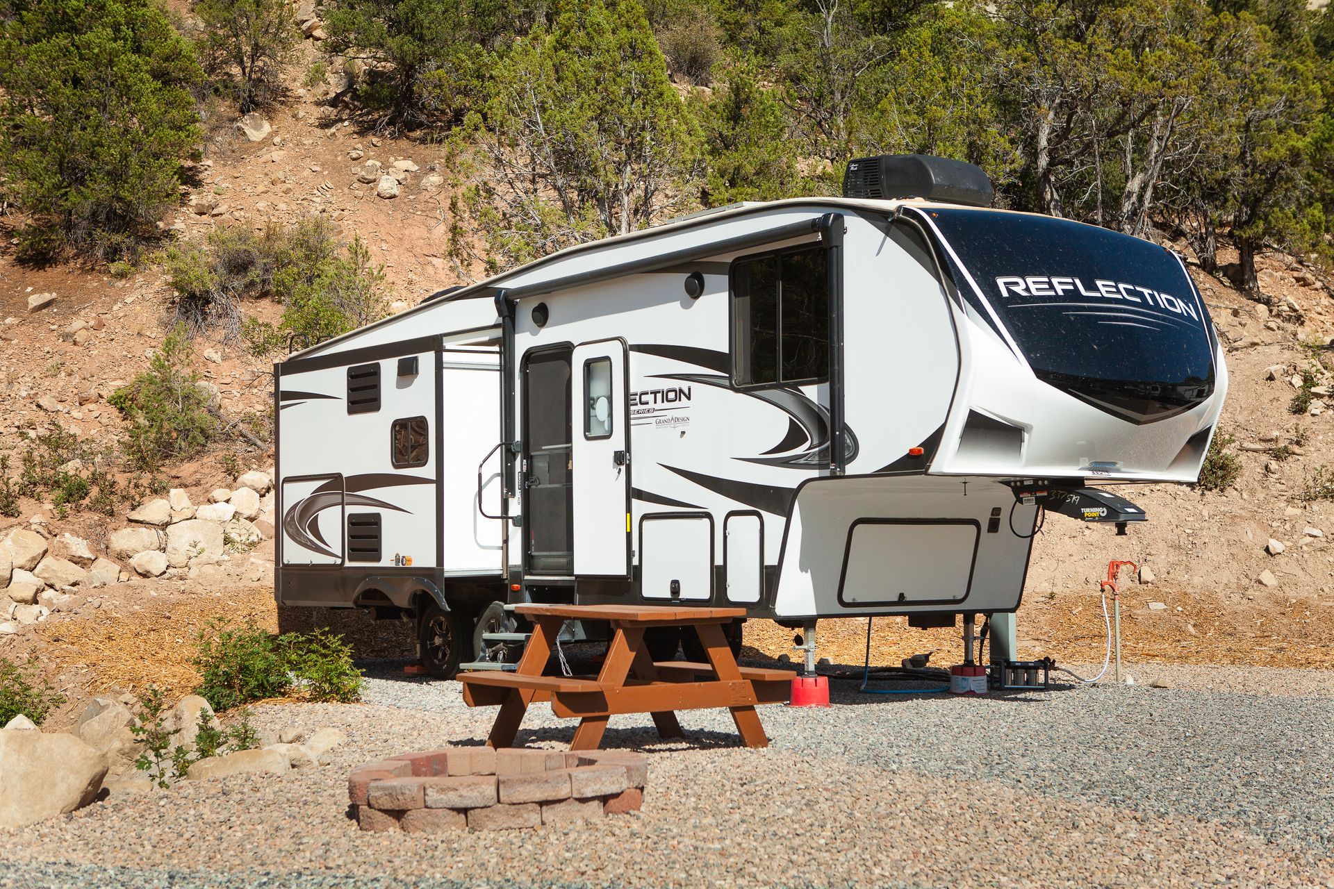 A rv is parked in a gravel area next to a picnic table.