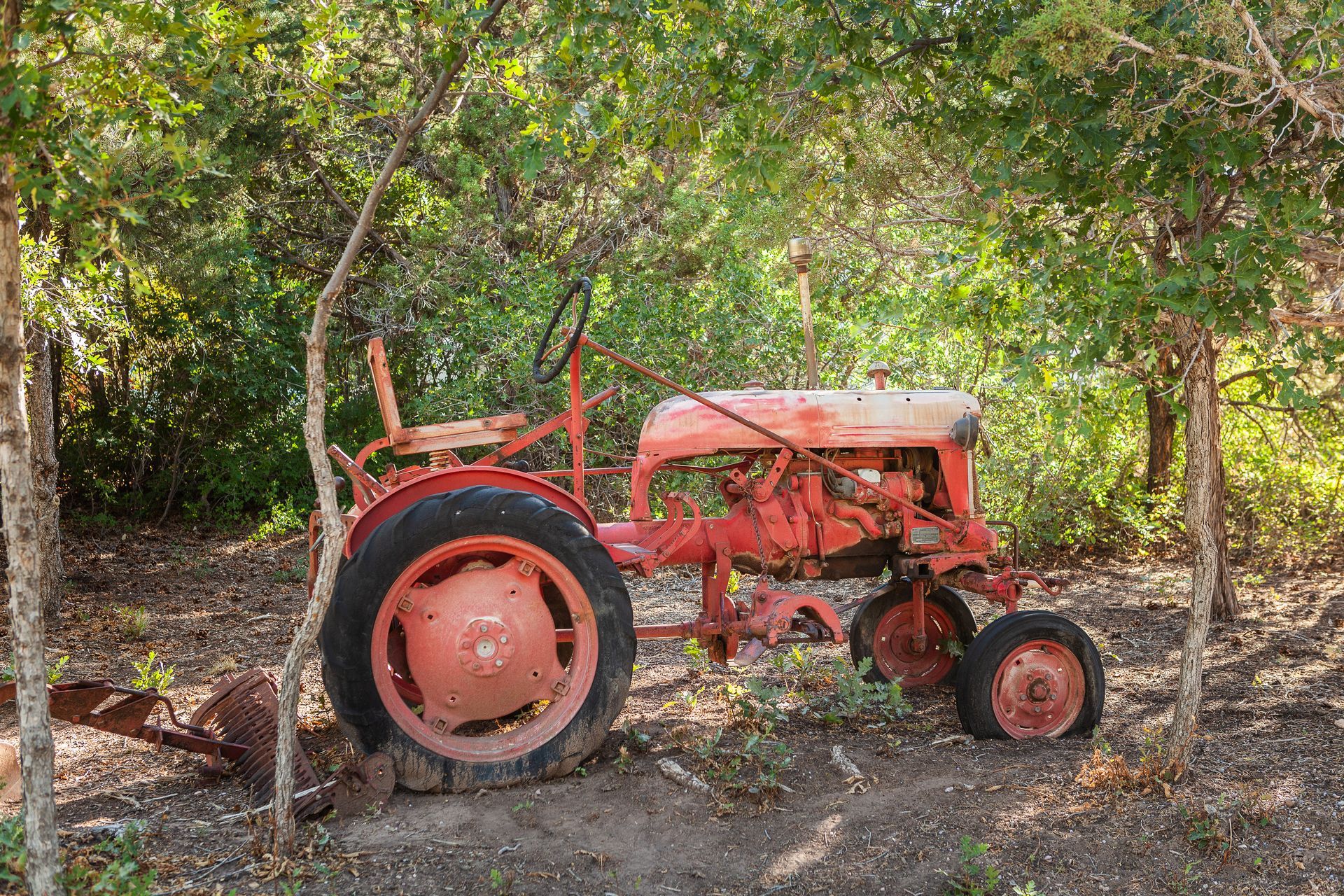 An old red tractor is parked in the woods.