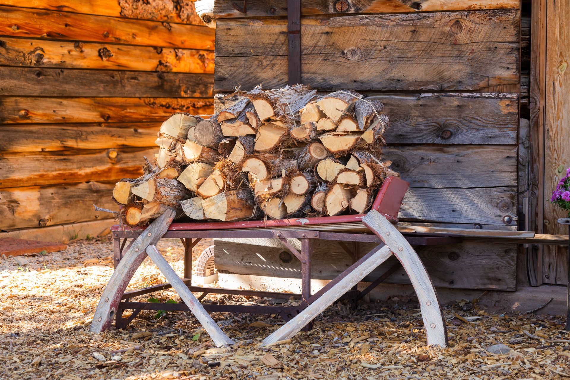 A pile of logs is sitting on a sled in front of a wooden building.