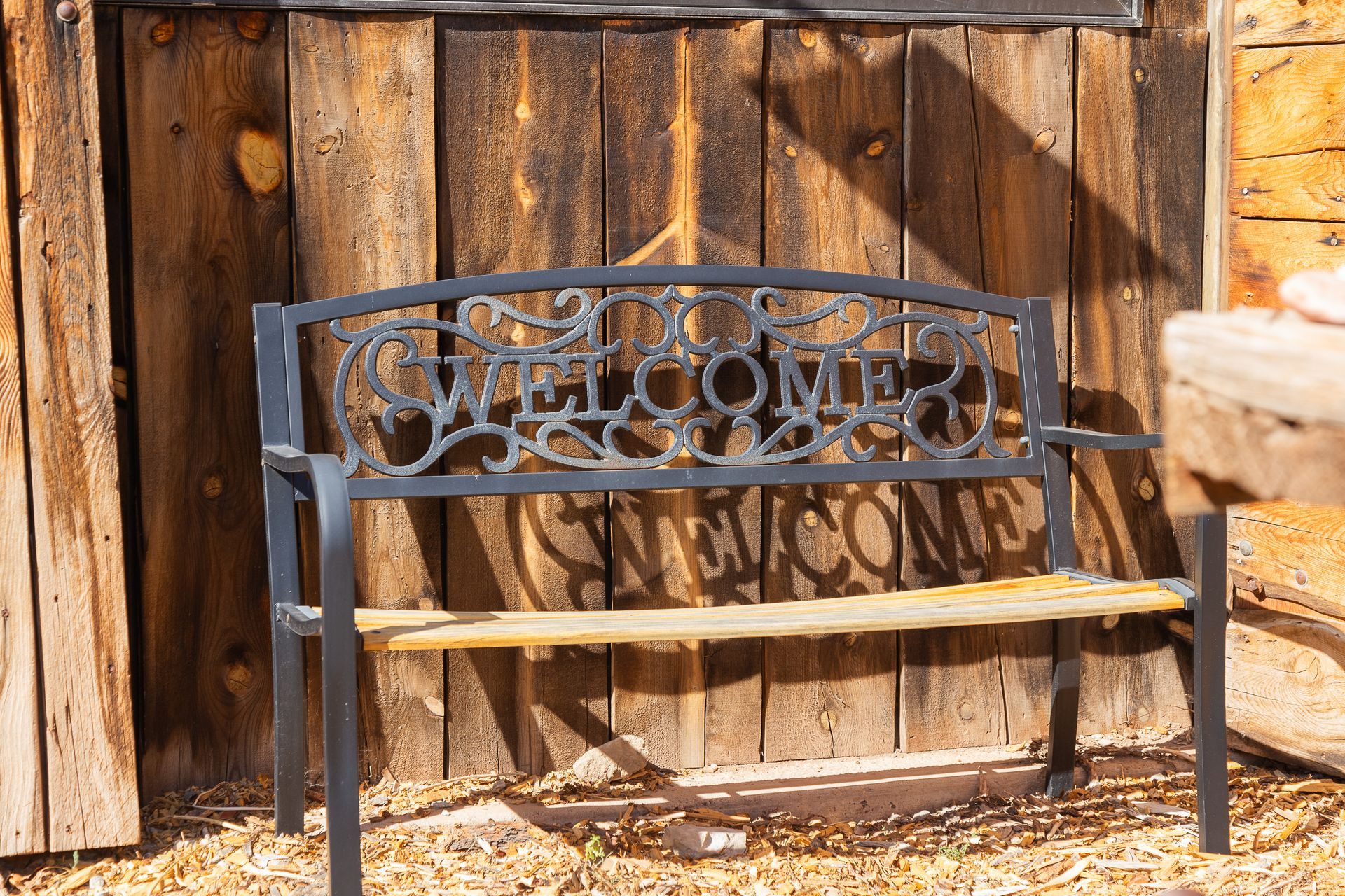 A bench with the word welcome on it is sitting in front of a wooden wall.