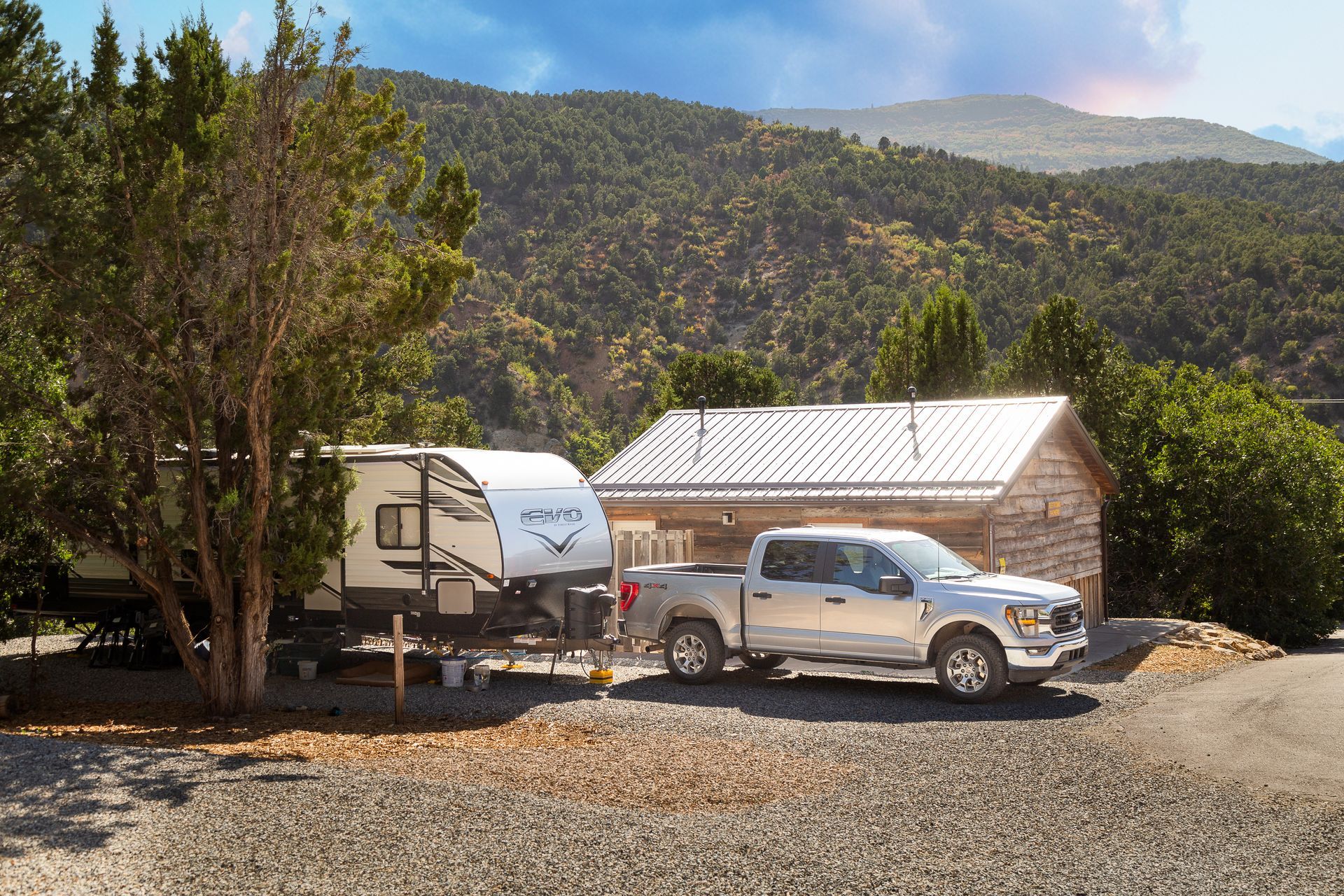 A truck is towing a trailer in front of a cabin.