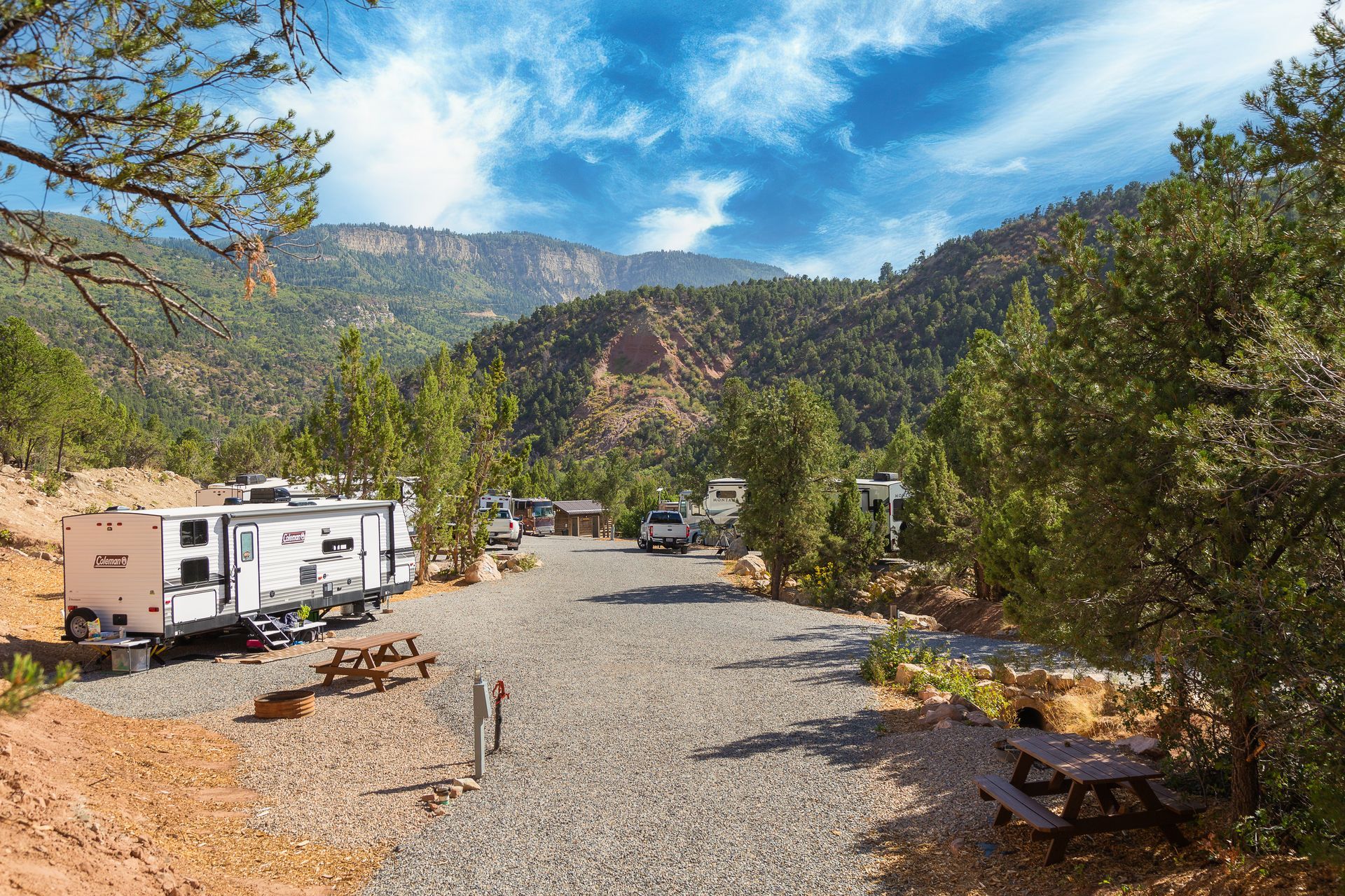 A rv is parked in a gravel lot with mountains in the background.