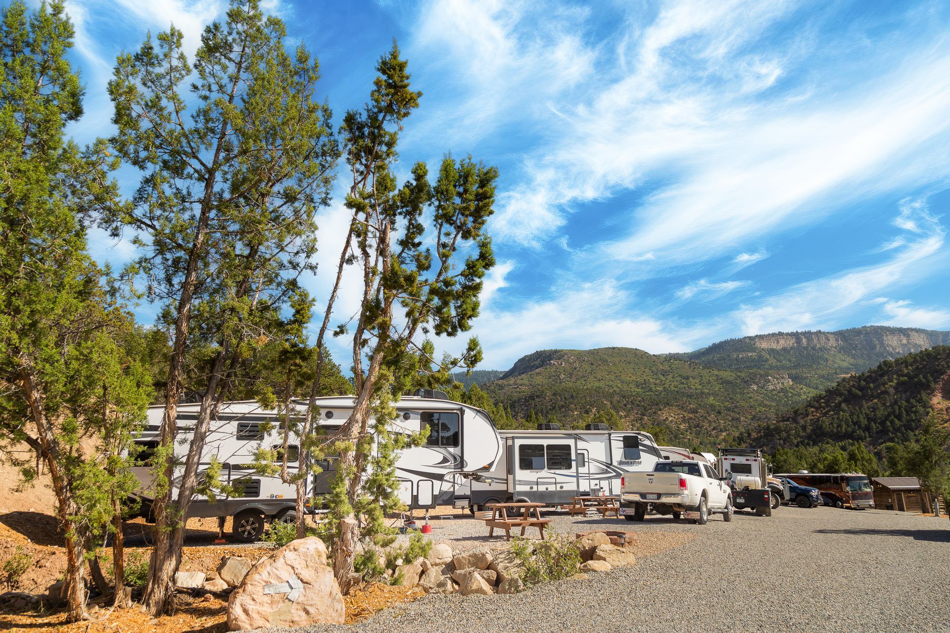 A group of rvs are parked in a gravel lot with mountains in the background.