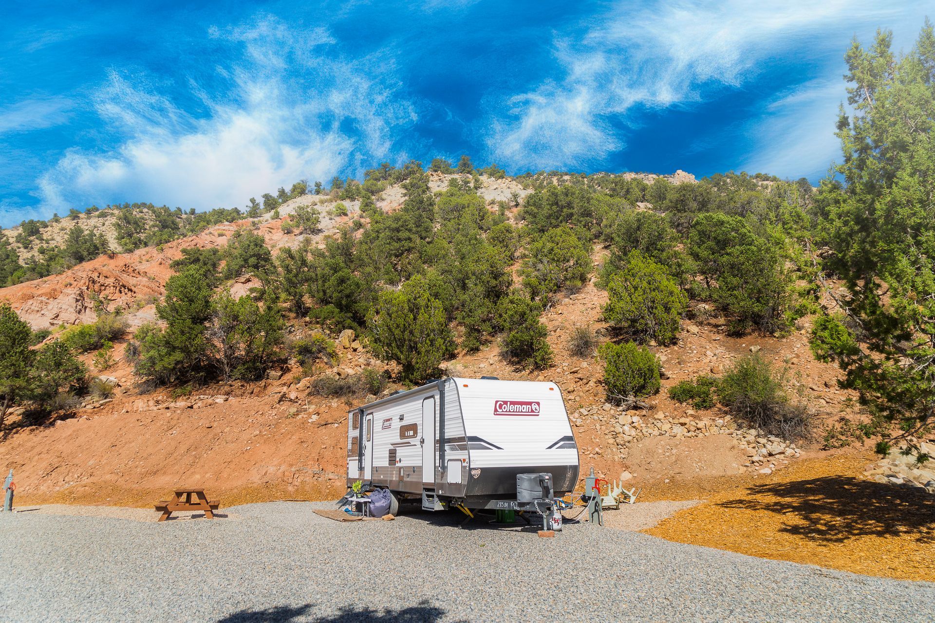 A rv is parked in a gravel lot next to a mountain.