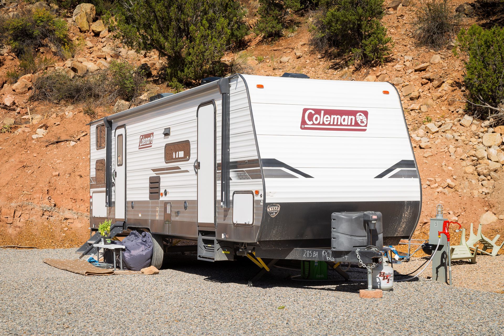 A coleman trailer is parked in a gravel lot.