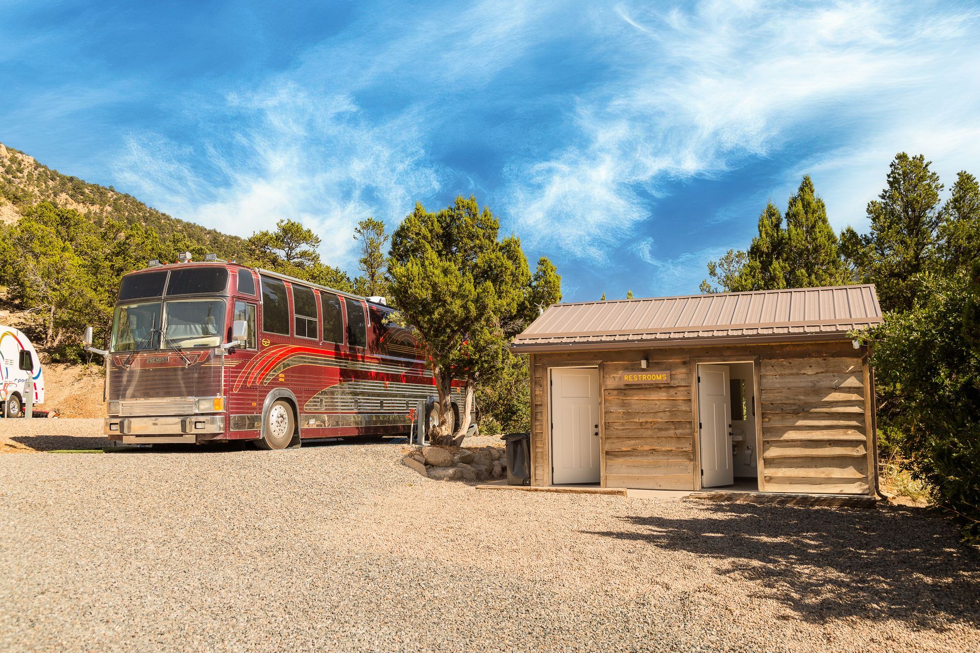 A red rv is parked next to a small wooden building.